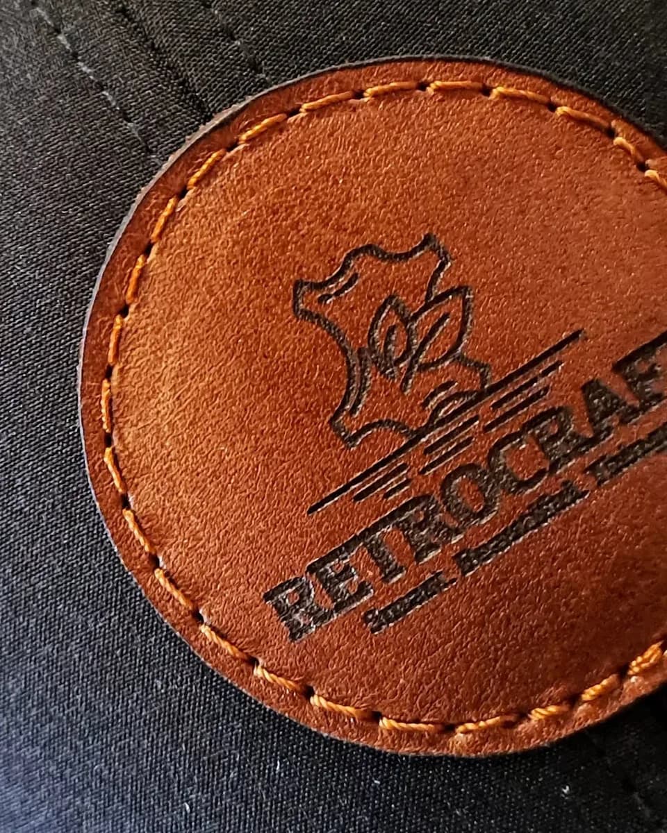 Close-up of a tan leather patch laser engraved with the RetroCraft logo, with a stitched border